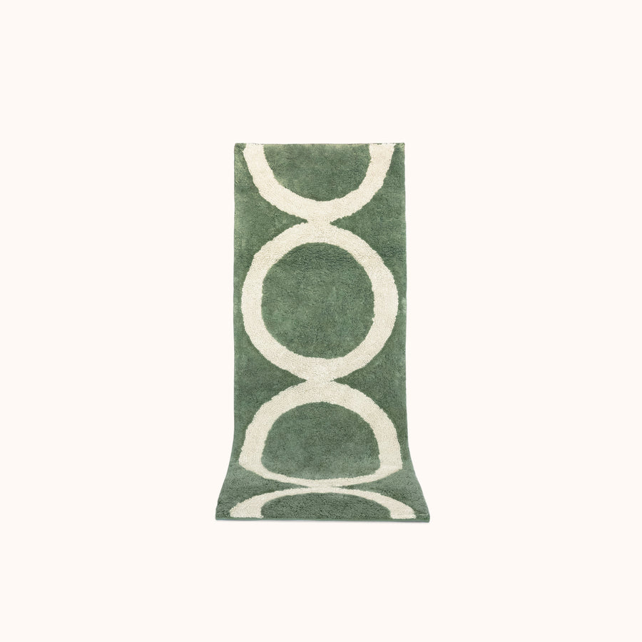 A green and tan geometric designed bath mat made of plush tufted cotton.