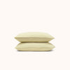 A set of stacked Límon / soft yellow organic matte sateen pillowcases a white background
