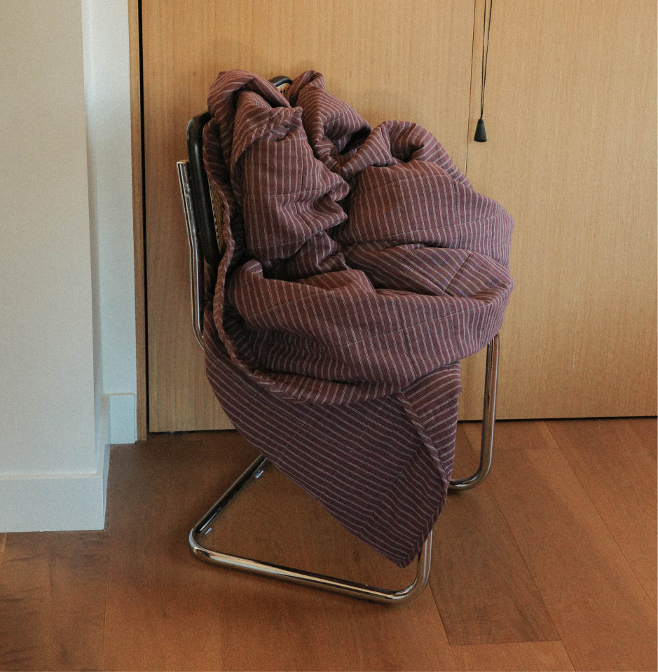 A maroon check quilt draped over a metal chair in a room with light wood flooring and doors.