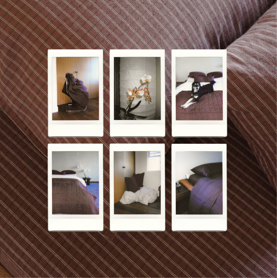 Six small instant-film-style photo prints arranged in a 2x3 grid on a maroon check bedspread. The photos show bedroom scenes, including a chair, flowers, a dog, and beds with purple bedding.
