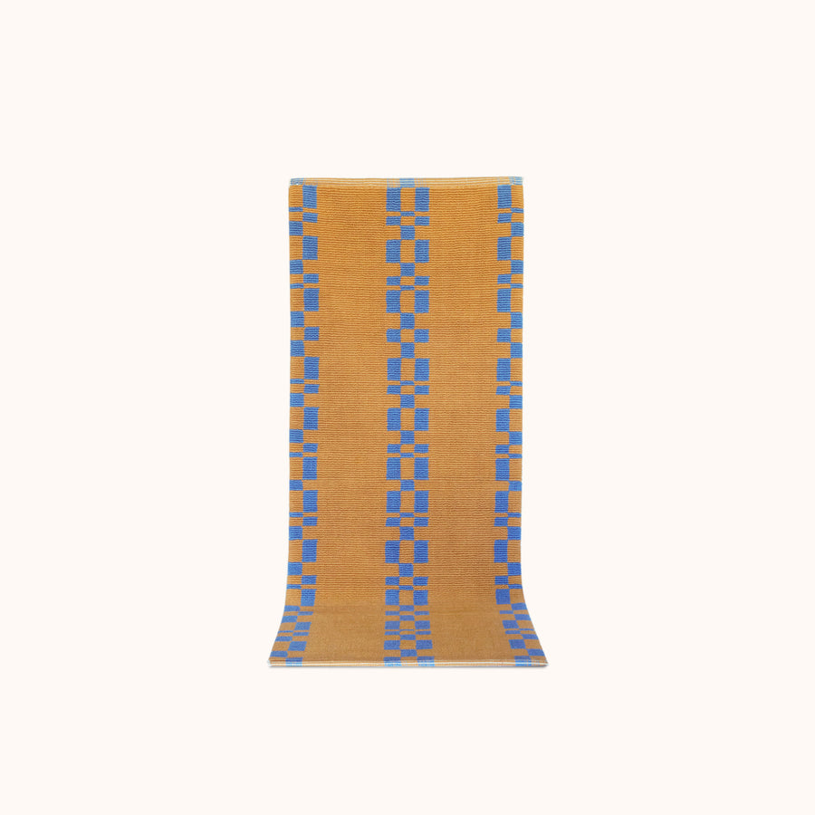 A runner  with a geometric pattern featuring blue squares on a camel brown background.