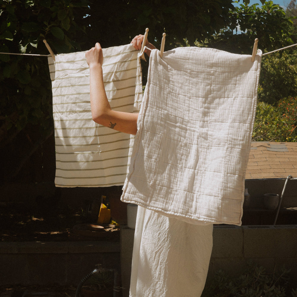 Person hanging neutral pillowcases on a clothesline