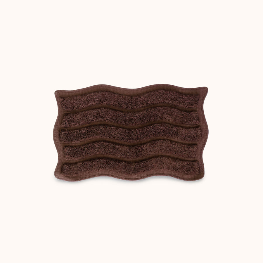 Brown textured bath mat with wavy pattern and alternating shag heights on a white background