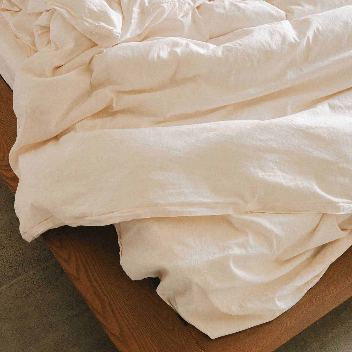 Close up on the corner of a wooden bed and rumpled cream / white sheets and a duvet cover