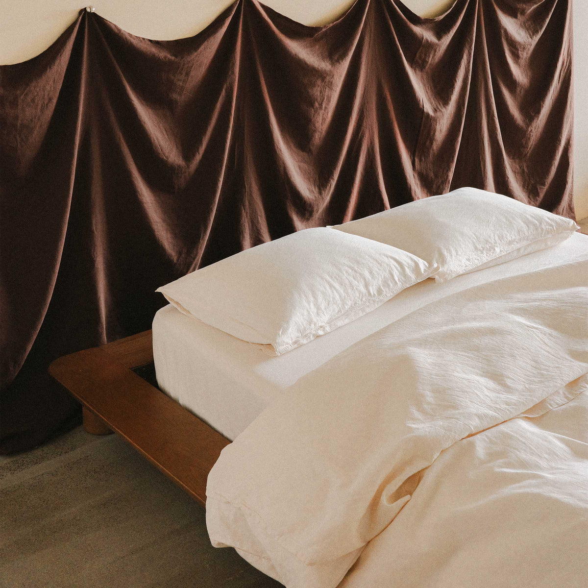 Close up of the top of a bed in a bedroom setting, the bed is creamy / white and the headboard is a purple fabric