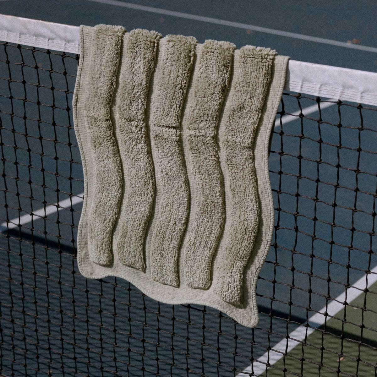 Green bath mat draped over a tennis net on a court