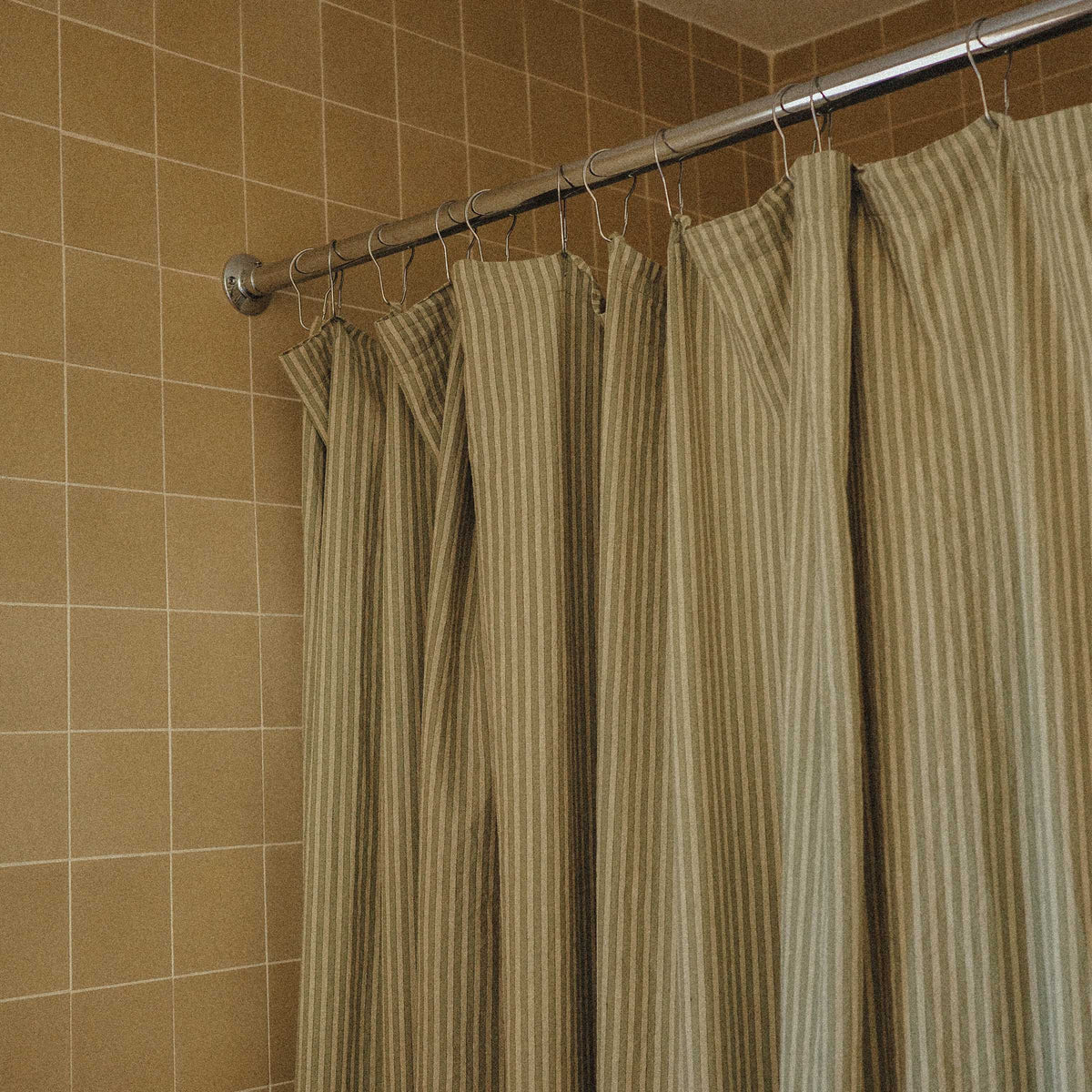 Striped shower curtain hanging on a rod against a tiled bathroom wall.