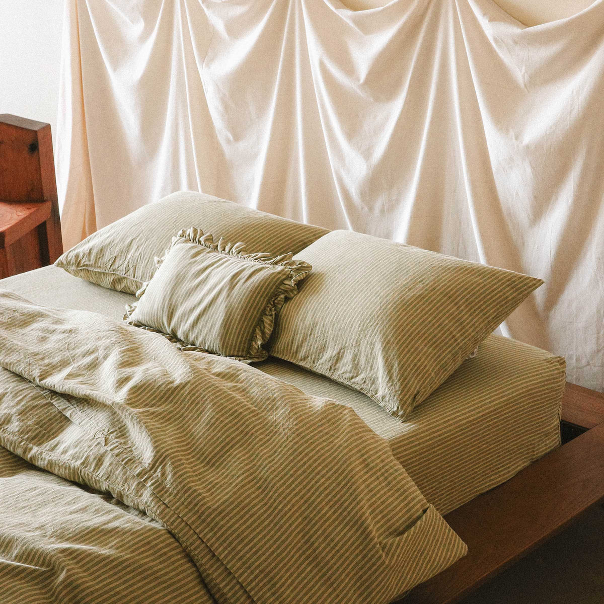 The top half of a bed with stripped sheets and a mini ruffle pillow
