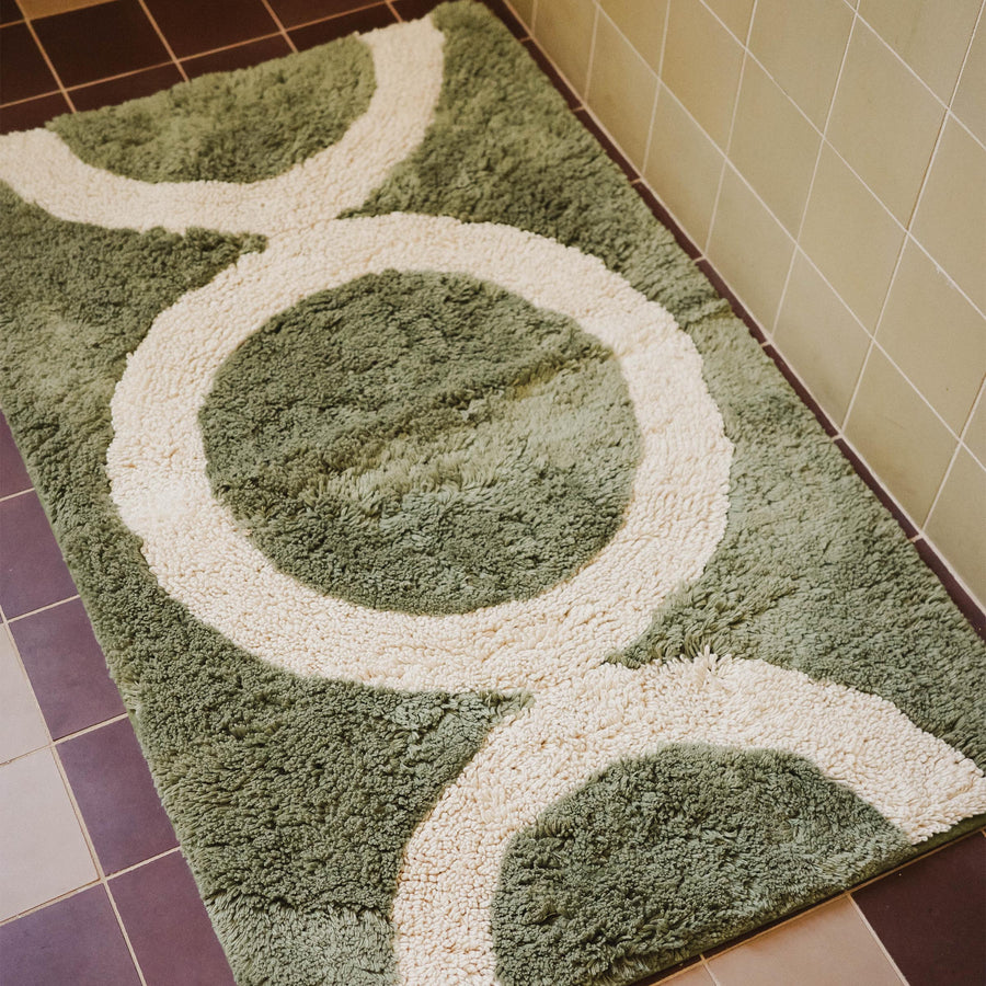 A green tufted bathmat with a beige circle pattern in a bathroom.