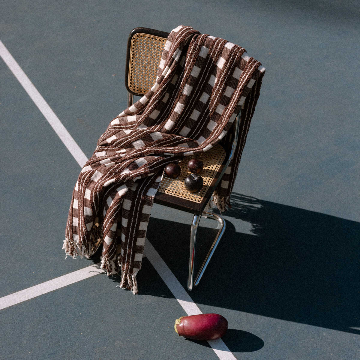 Checkered blanket draped over a chair on a tennis court with an eggplant beside it.