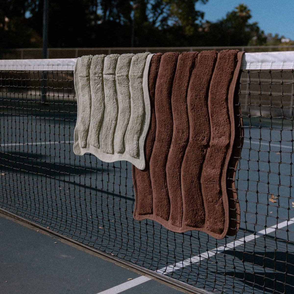 Two bath mats, one green and one brown, hanging on a tennis net.