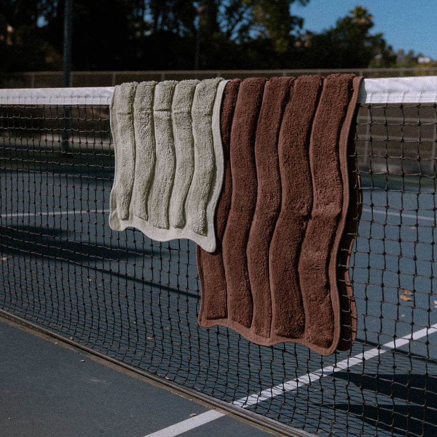 Two bath mats, one green and one brown, hanging on a tennis net.
