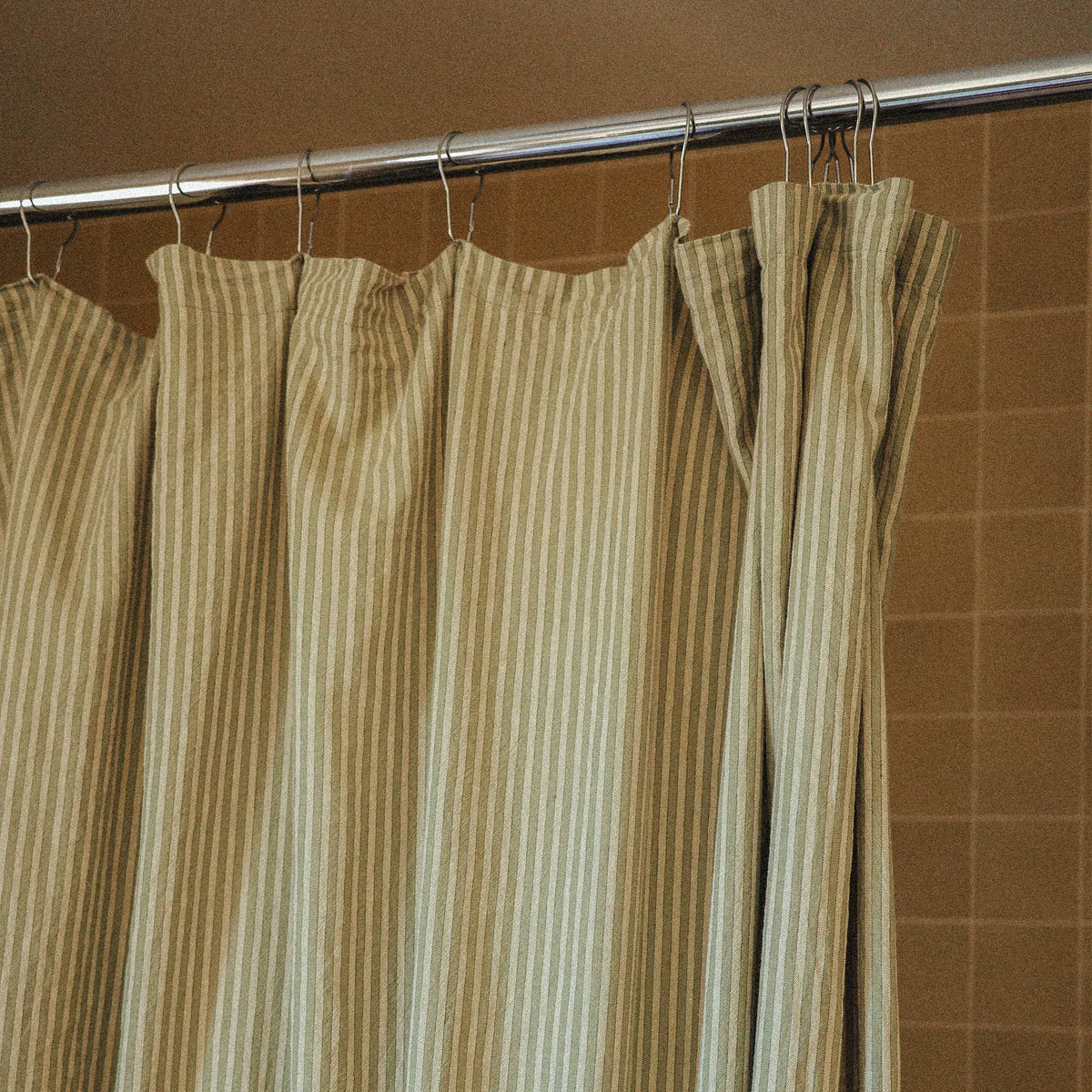 Striped shower curtain hanging on a rod against a brown tiled wall.