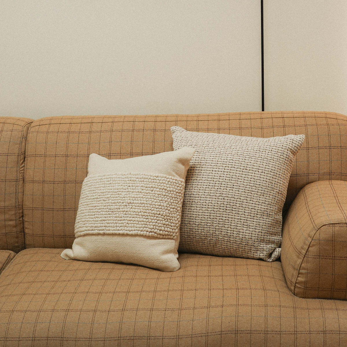 A cream textured throw pillow and a tan patterned throw pillow on couch.