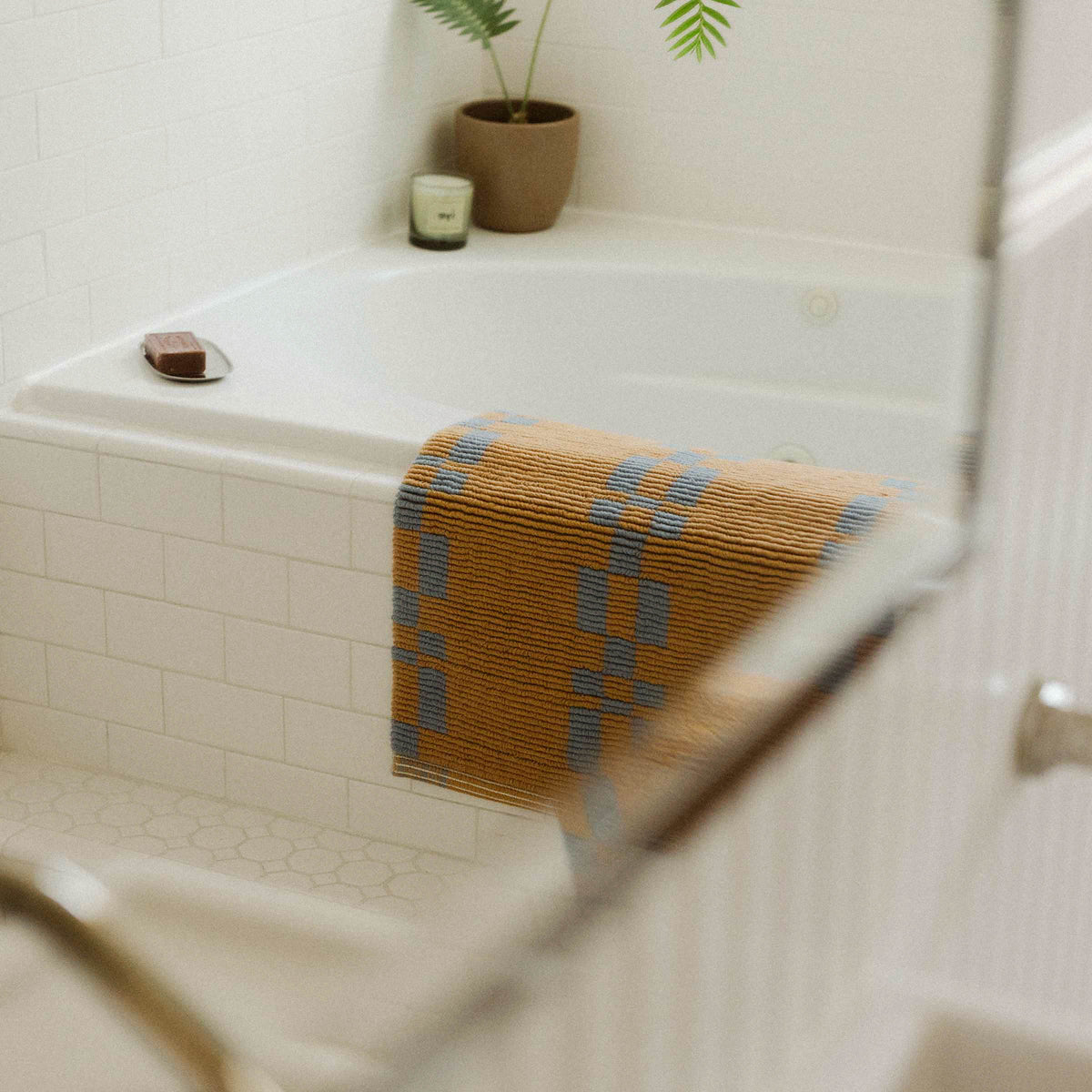 A brown and blue bathmat draped over the edge of a white tile tub.