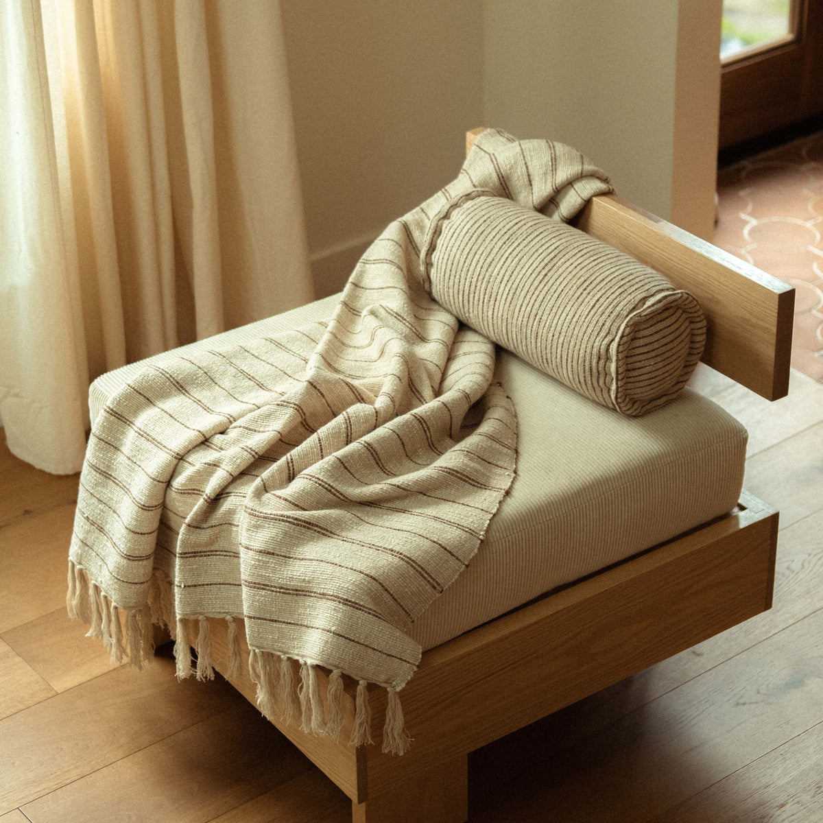 A modern accent chair with the Pia bolster and Pia throw blanket draped casually. 