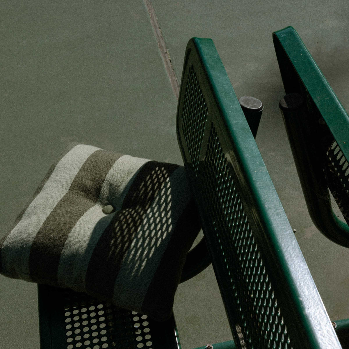 Close-up of a striped green throw pillow on a green bench on a tennis court.