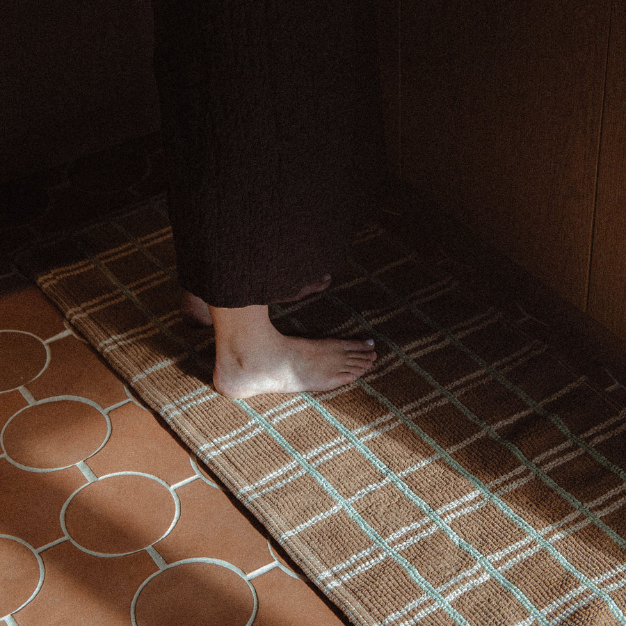 A person standing on brown bathmat with green and tan intersection stripes in a kitchen.