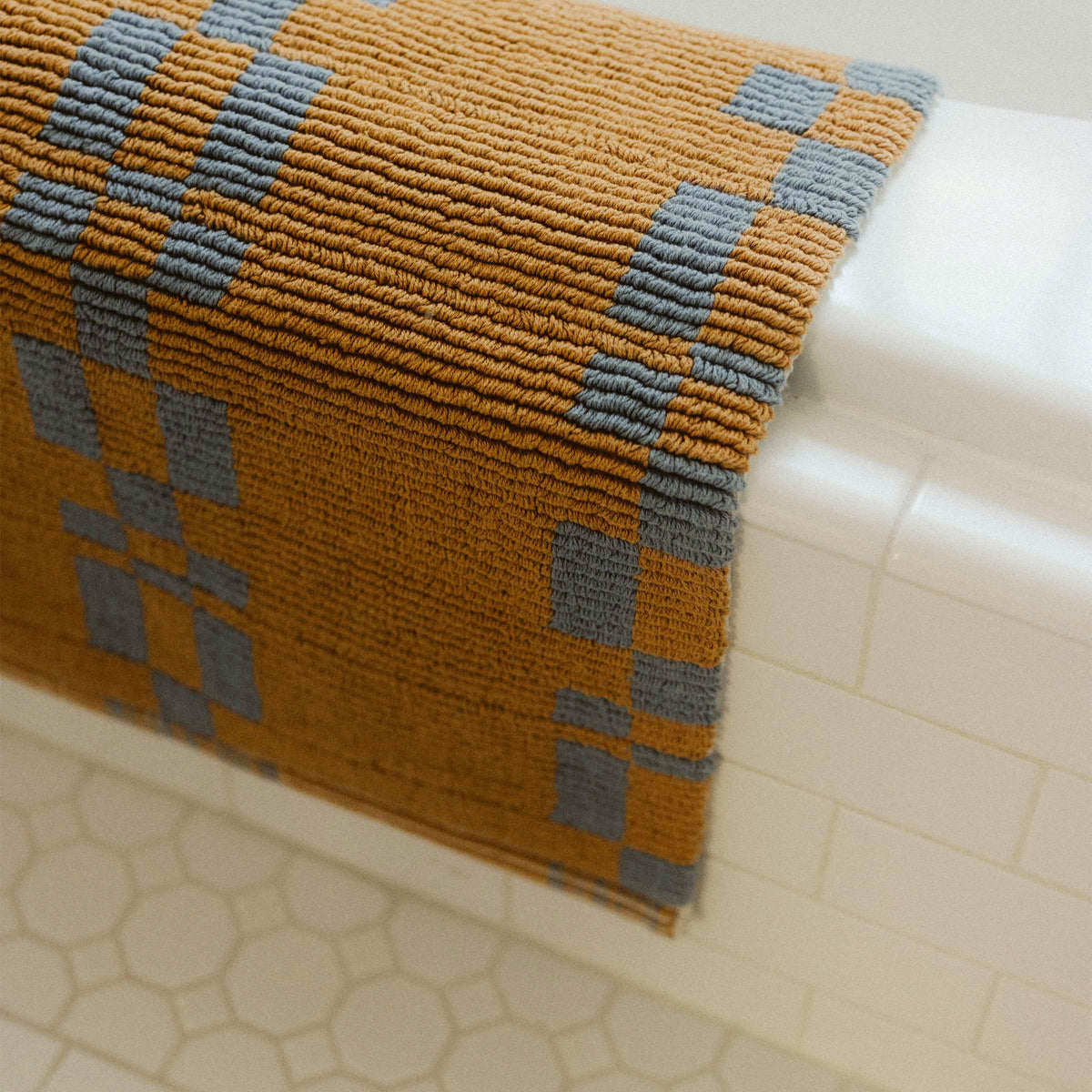 a blue and brown bathmat draped over the edge of a whit tiled bathtub. 