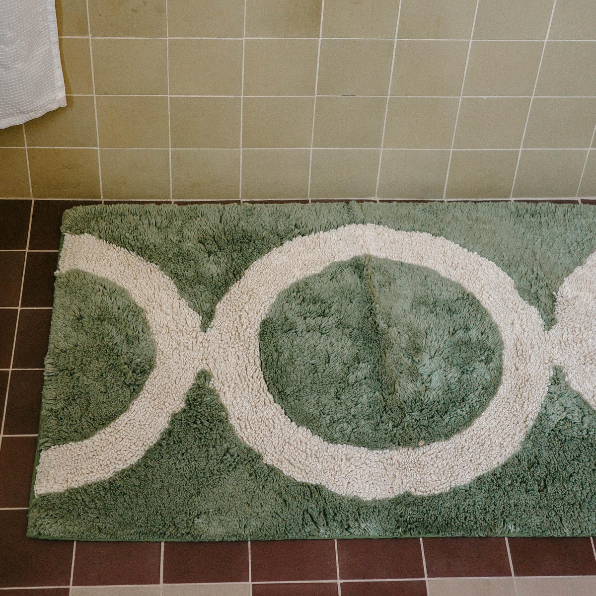 Close up of a green tufted bathmat with a tan circle pattern in a bathroom.