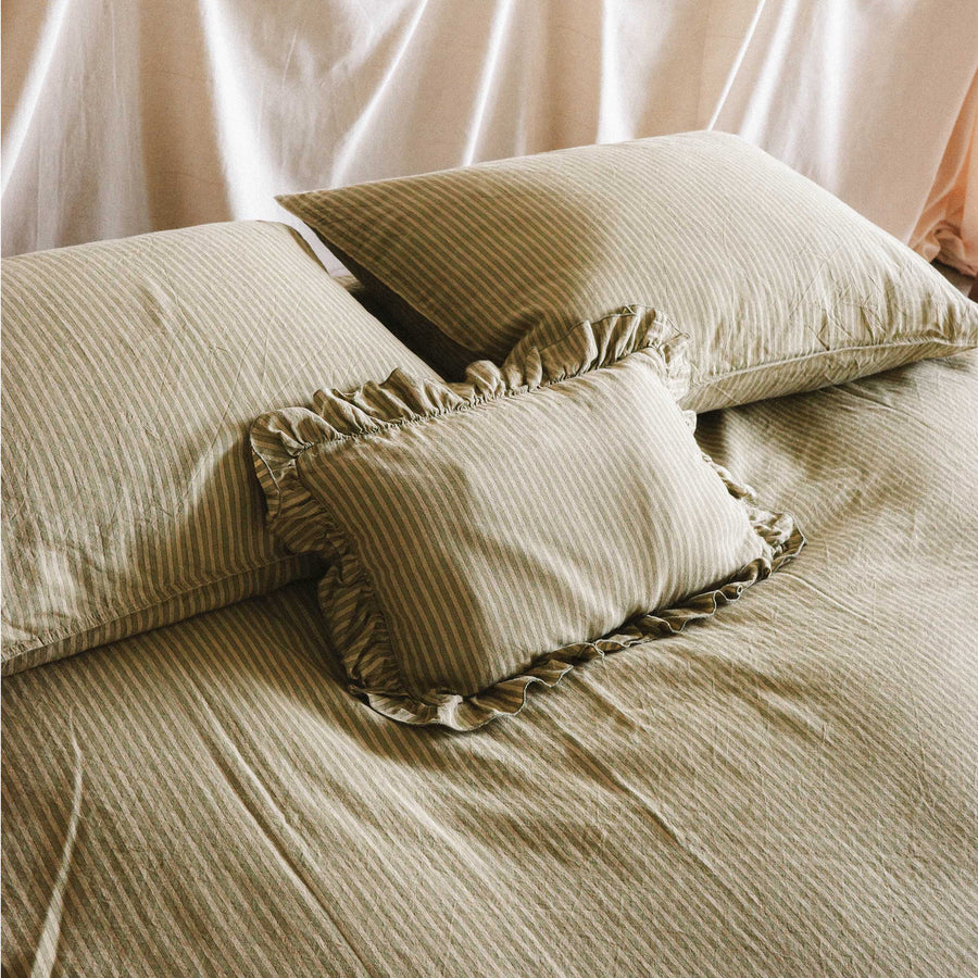 Close up of the top half of a bed with stripped green sheets and a mini ruffle pillow in a bright bedroom setting