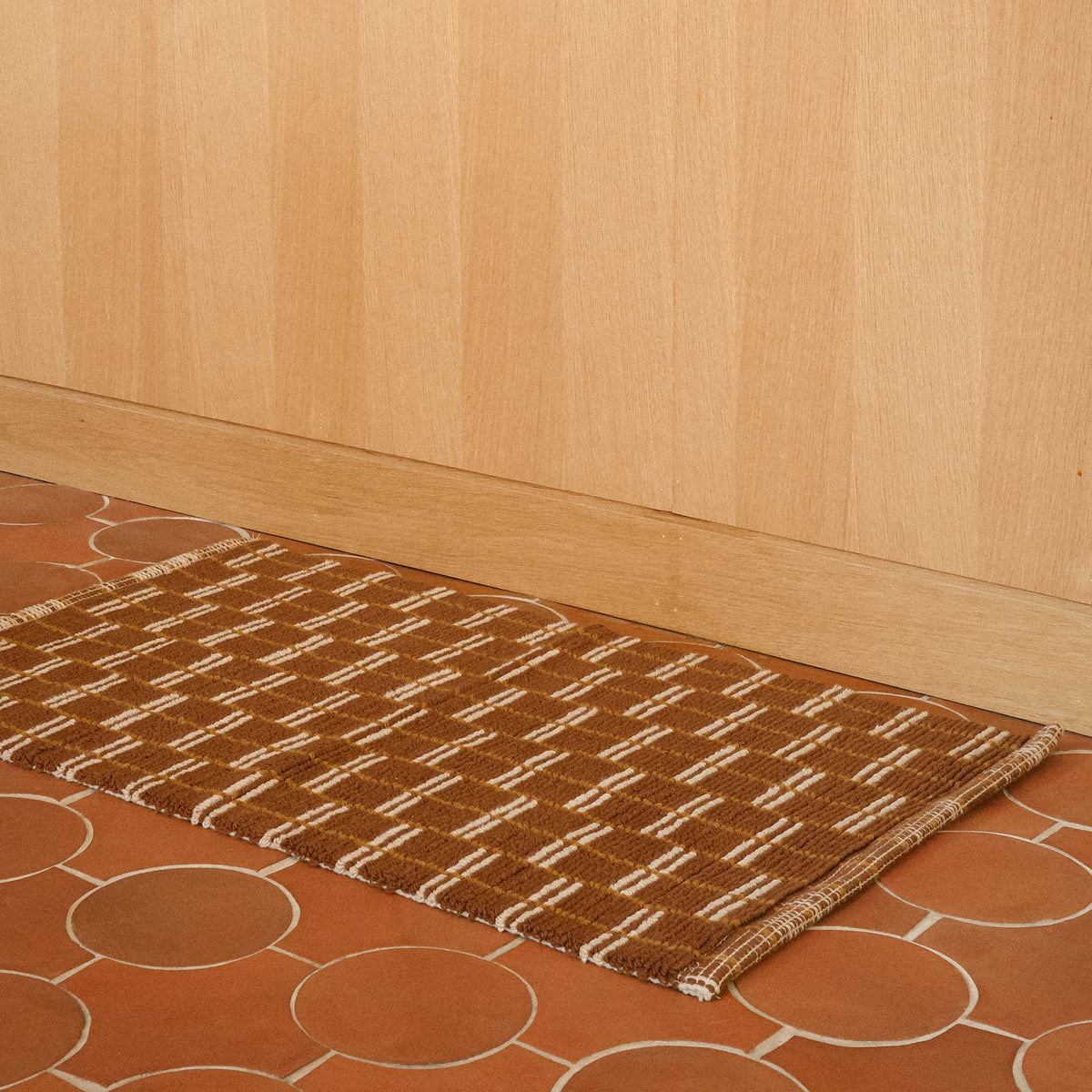 A brown bathmat constructed of tiny loops with a brown and tan geometric pattern.