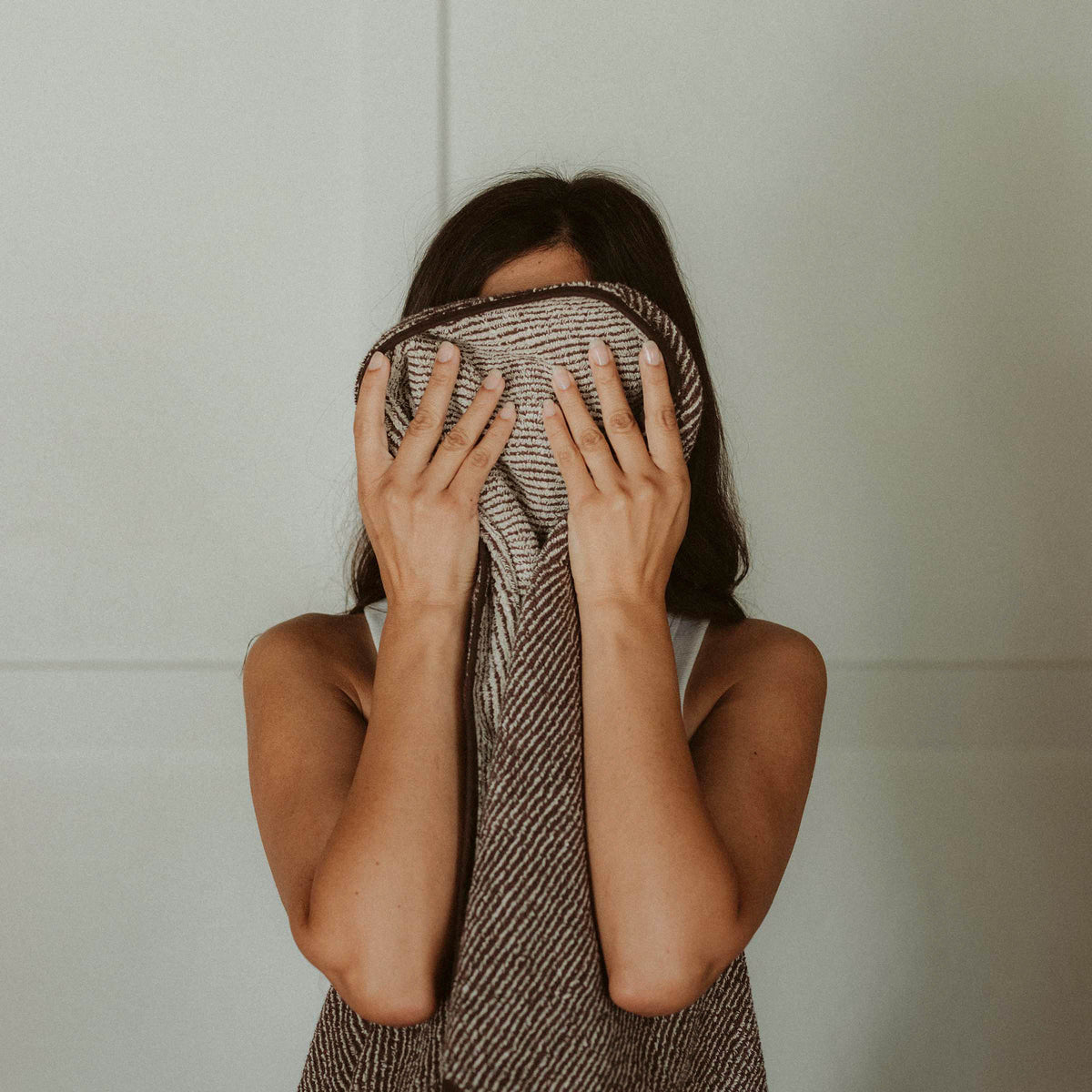 A woman wiping her face with a brown and tan striped bath towel.