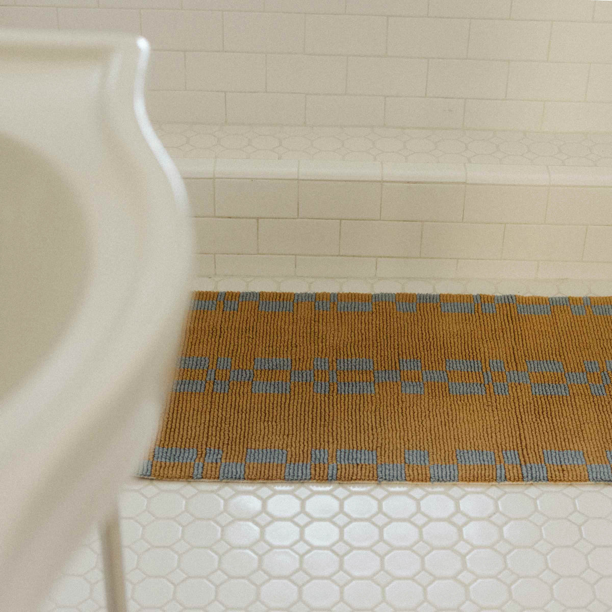 a brown bathmat with a blue geometric pattern on a white tile bathroom floor.
