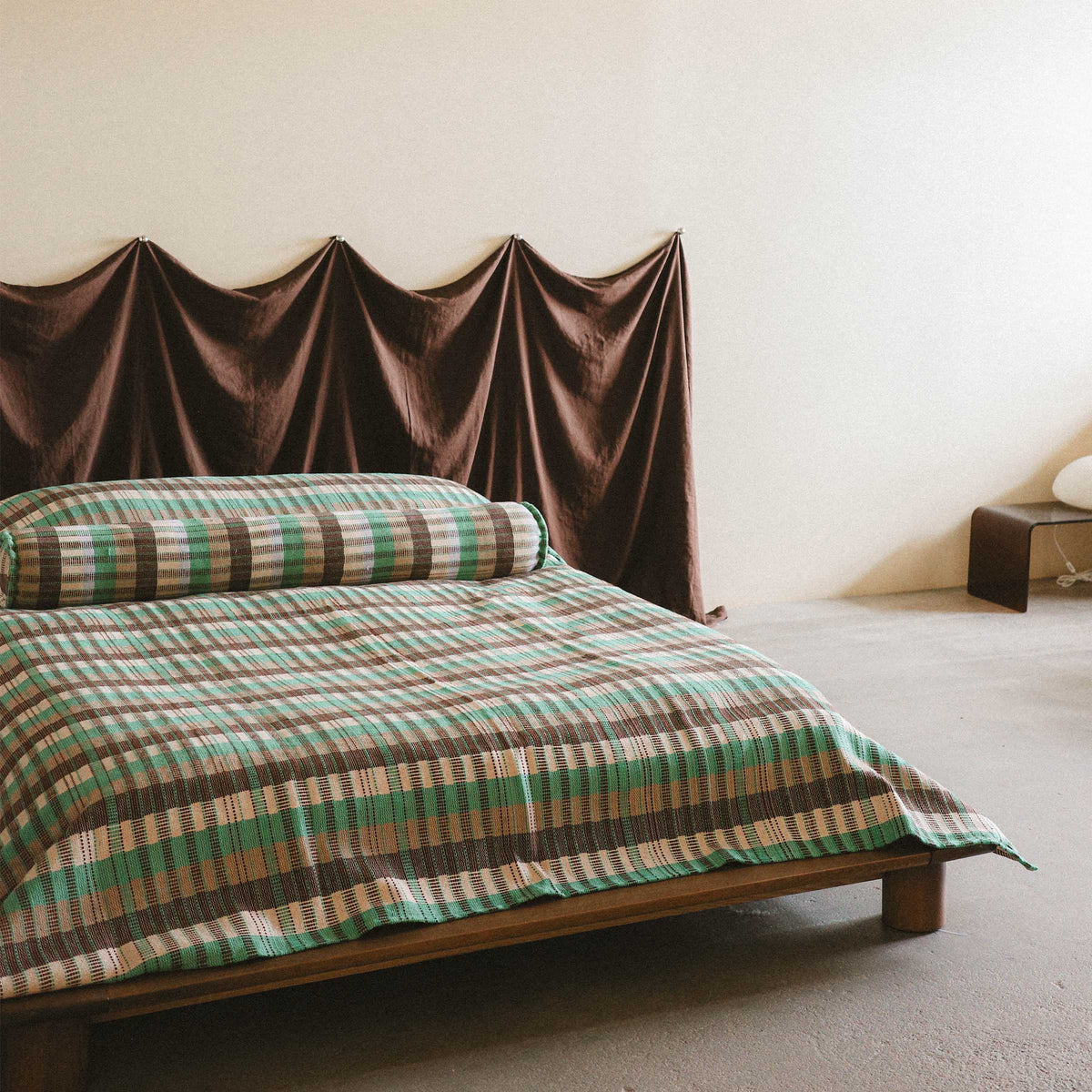 A bright and modern bedroom setting with the checkered Yara bed cover on a low bed styled with the Yara bolster against a brown fabric headboard 