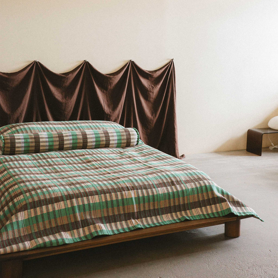 A bright and modern bedroom setting with the checkered Yara bed cover on a low bed styled with the Yara bolster against a brown fabric headboard 