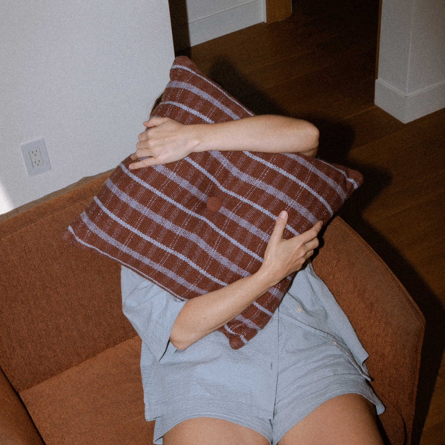 Person holding a brown and lavender striped pillow on a couch