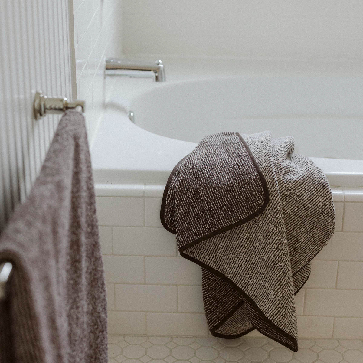 Brown and tan striped bath towel draped over the edge of a white tile bath tub.
