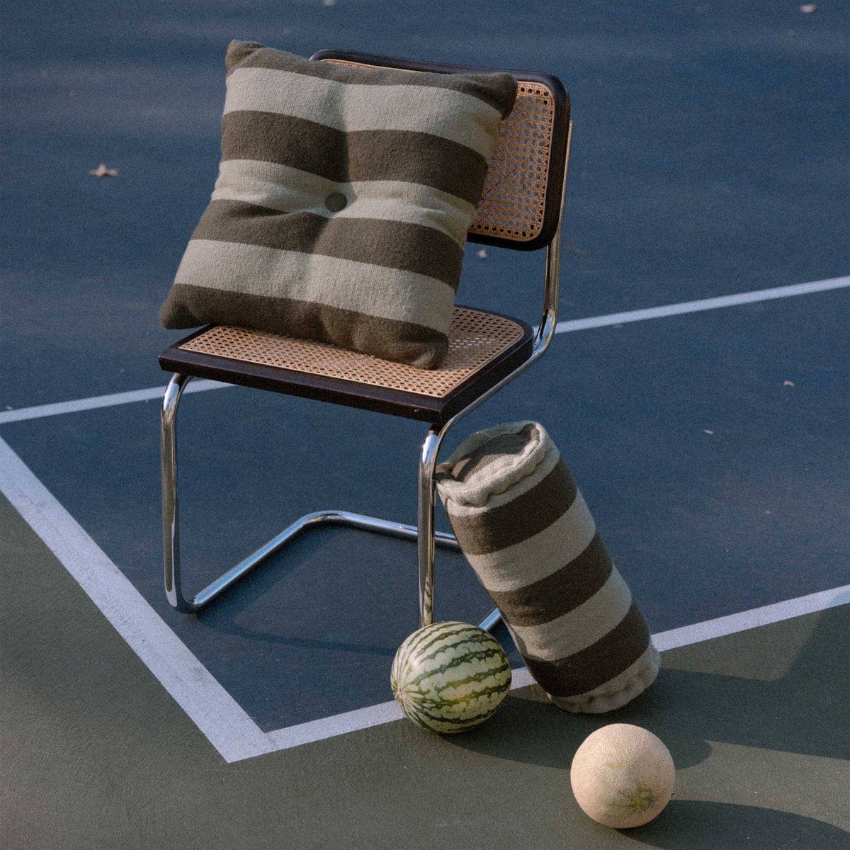 Chair with green striped throw pillow and bolster on a tennis court