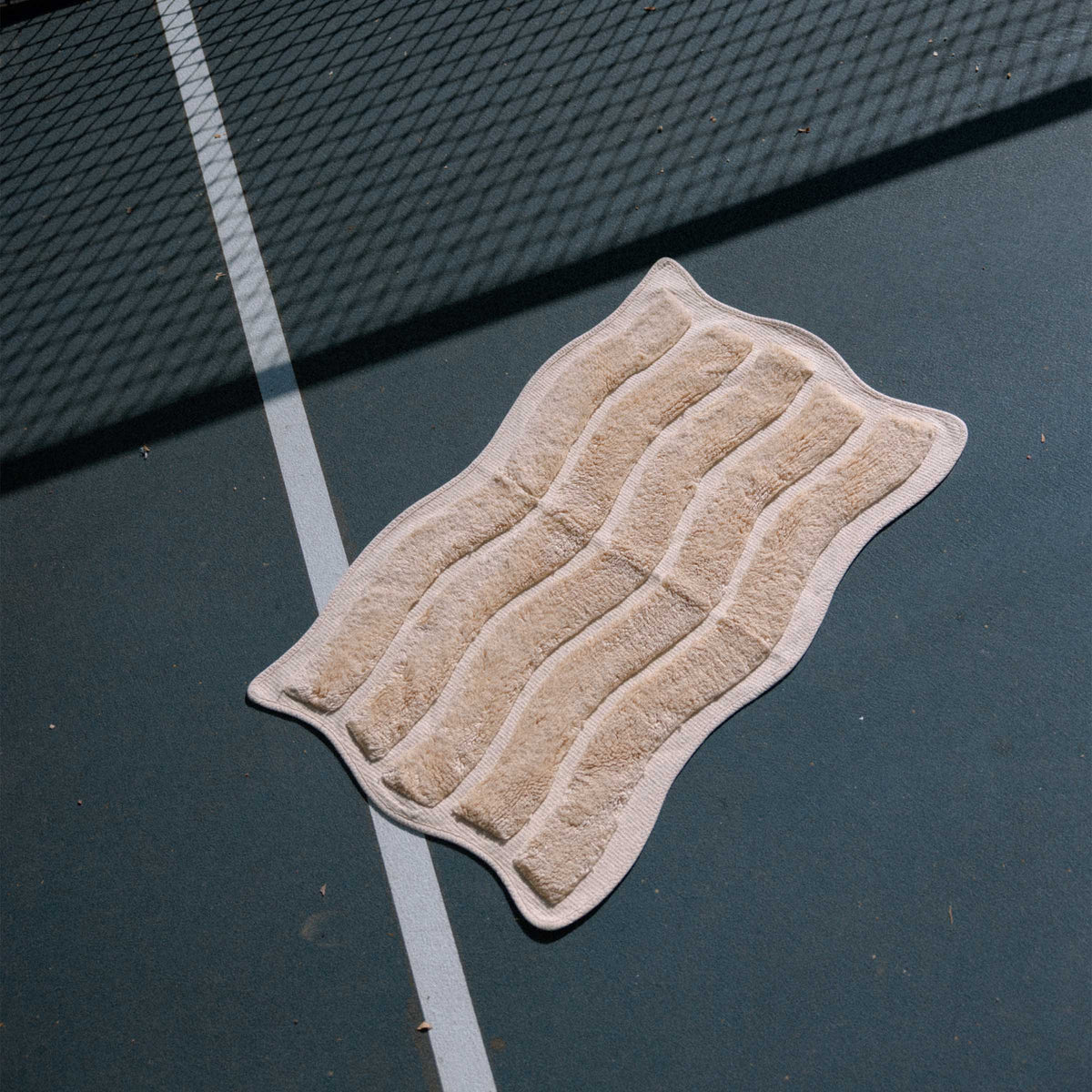 yellow bath mat with wavy pattern on the dark surface of a tennis court.
