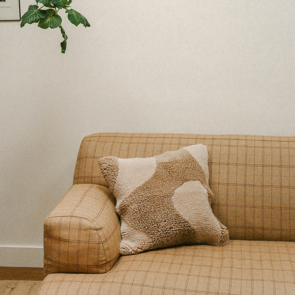 A living room setting with a checkered tan sofa with the Otis pillow resting. The Otis is a square throw pillow with an organic design in cream and beige.