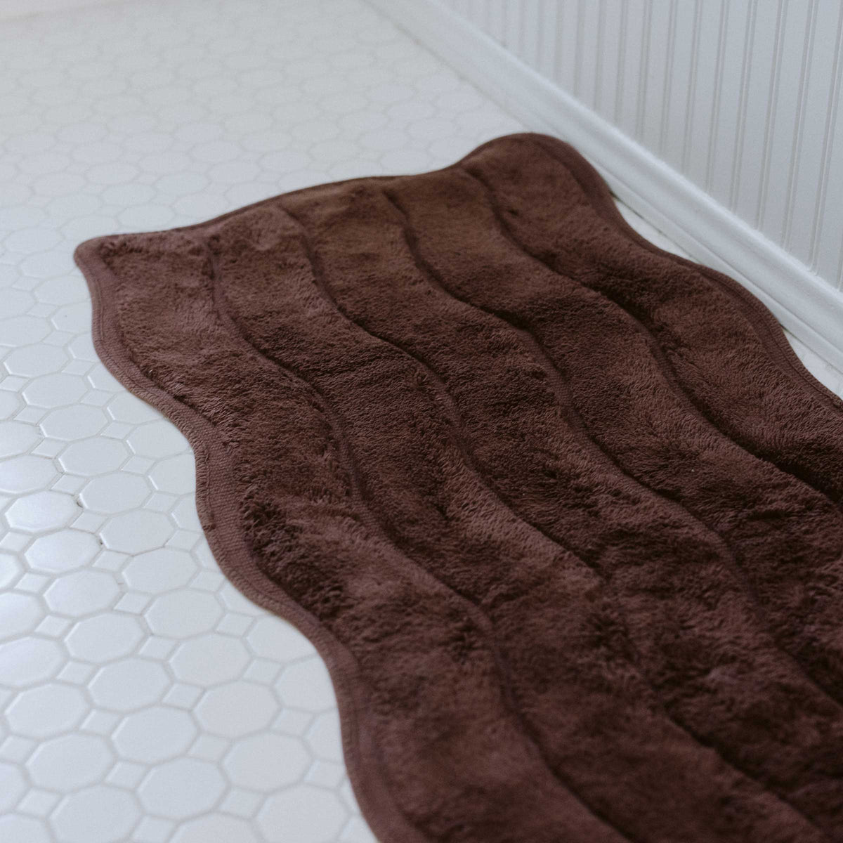 Brown textured bath mat on a white tiled bathroom floor