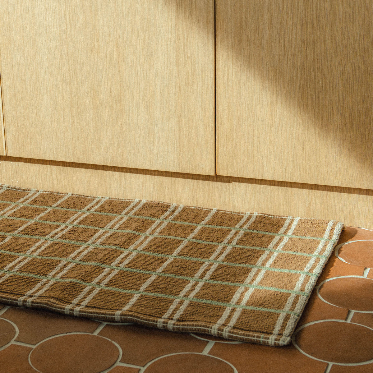 Close up of a brown mat with a green and tan geometric pattern on a terracotta tile floor.