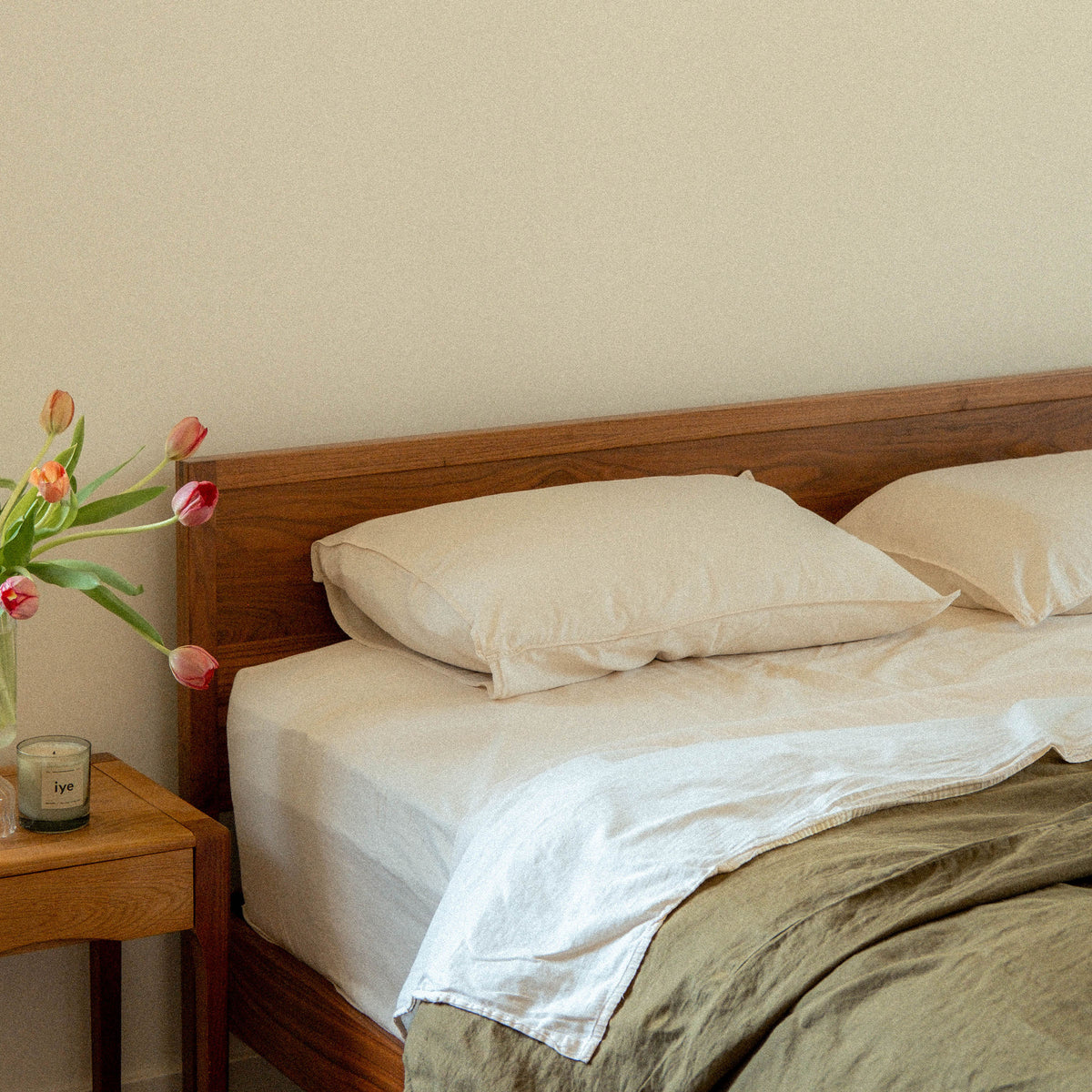 A bed with two Oat pillows and sheets with a green duvet cover in a bedroom setting 