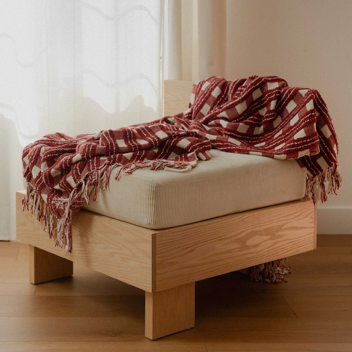Red and cream pattern blanket draped over a chair in a room with a white curtain.