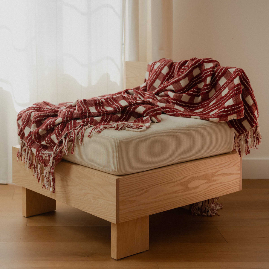 Red and cream pattern blanket draped over a chair in a room with a white curtain.