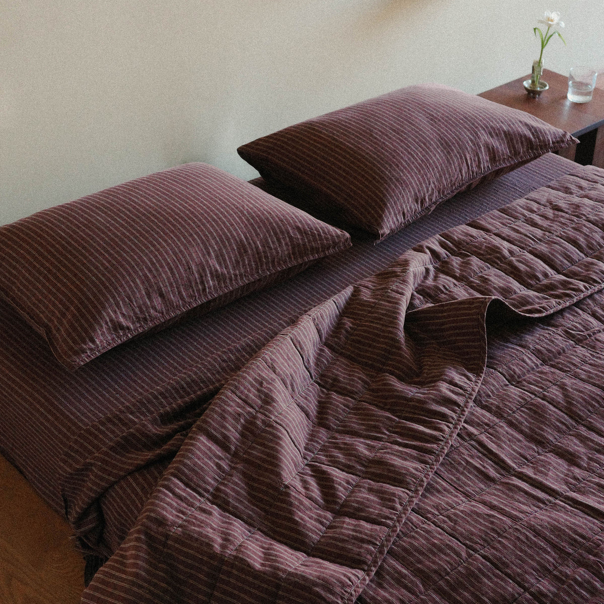 Brown striped quilt / bed cover and pillows on a bed with a nightstand adorned with a blooming white flower and glass of water