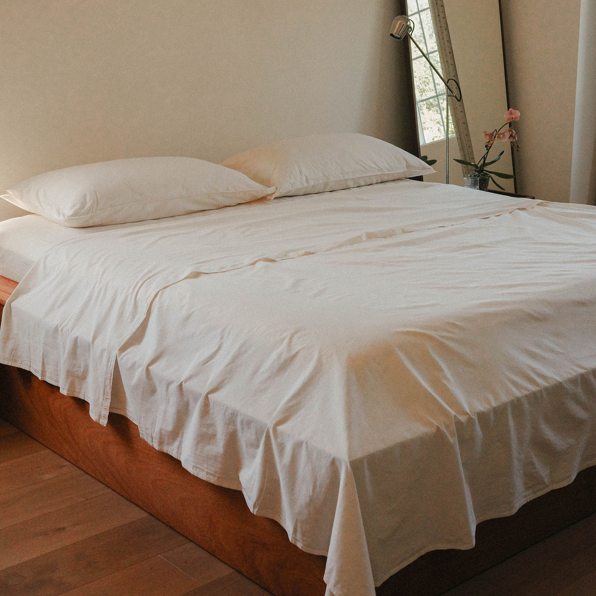 Bed with cream bedding in a room with a mirror and curtains.