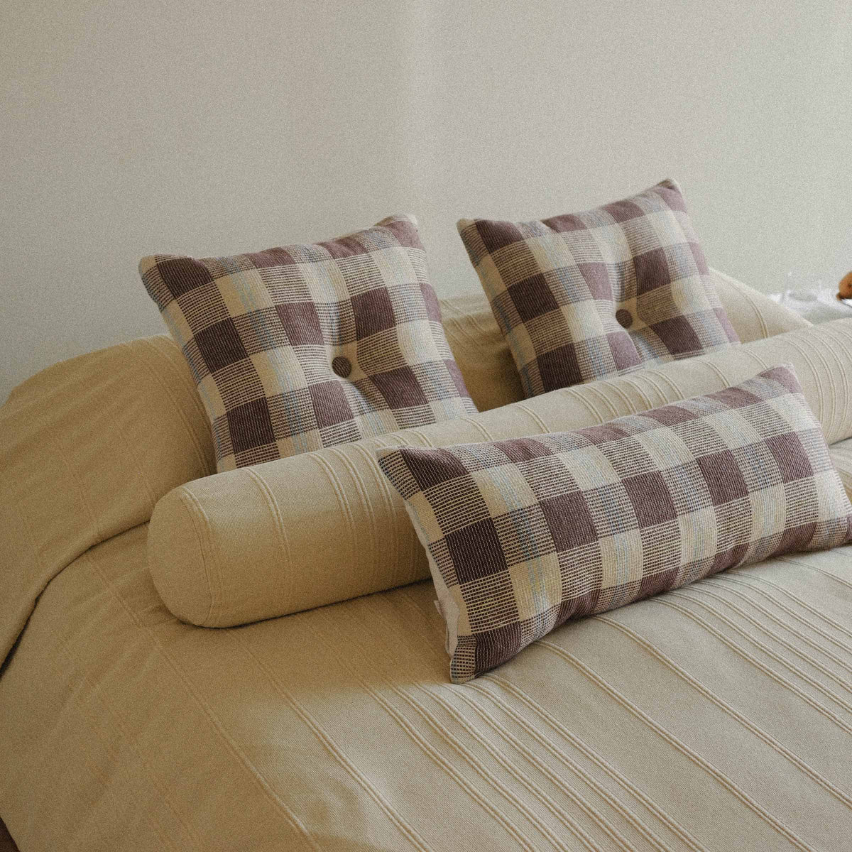 A bed neatly made with a yellow bed covering and checkered throw pillows