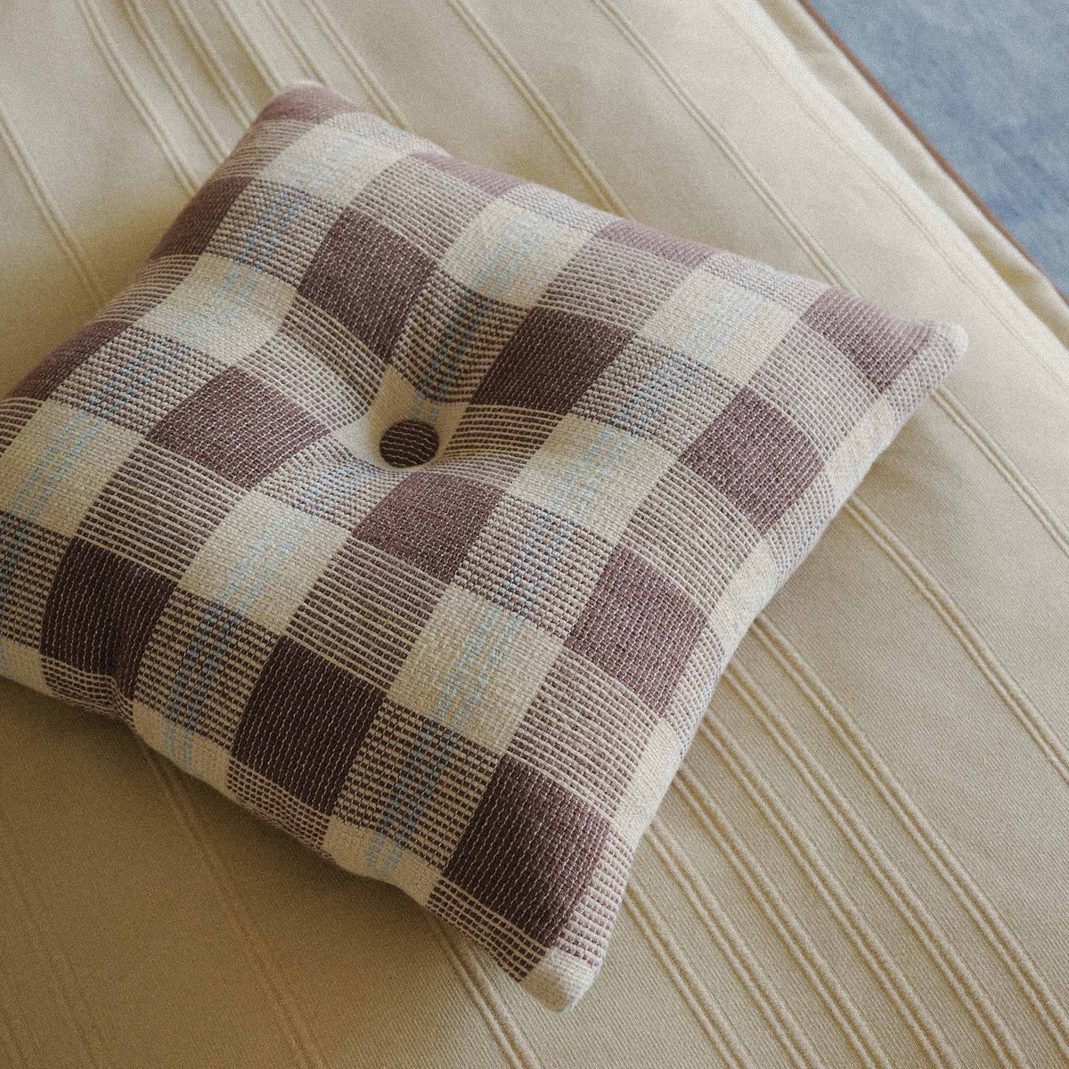 Close up of the Mina throw pillow which has a button in the middle and is checkered patterned