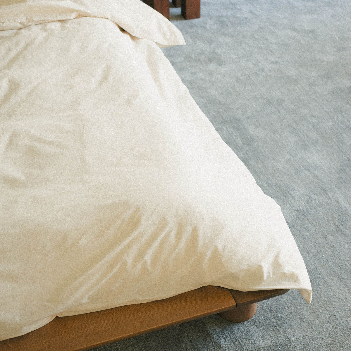 Close-up of a cream duvet cover on a bed with a blue carpeted floor.