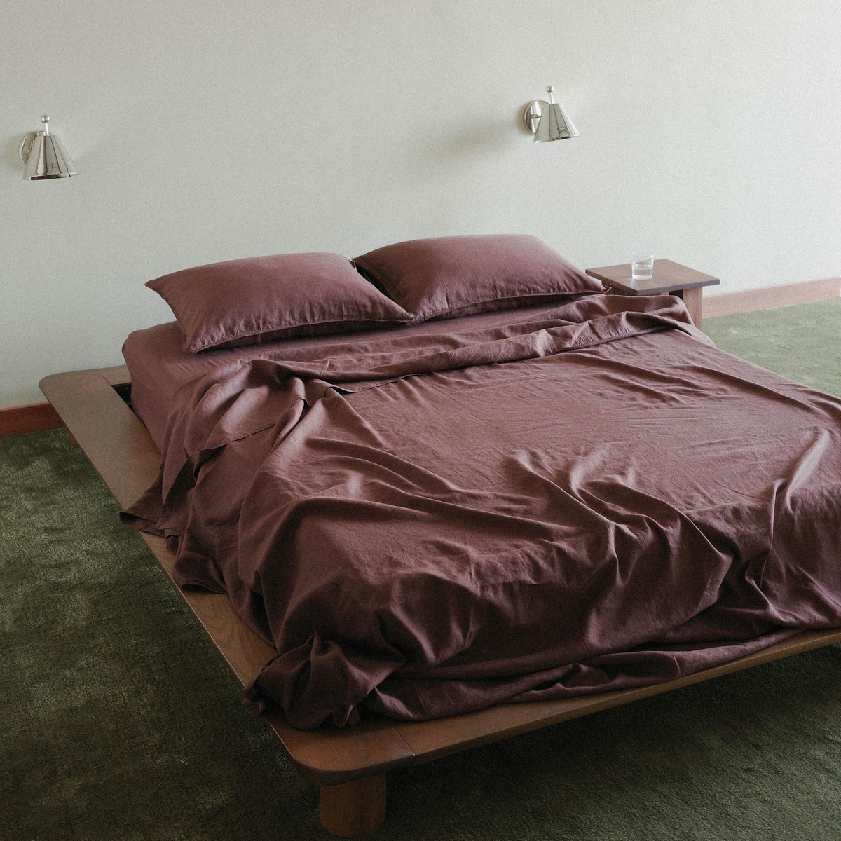A wood bed with purple / brown sheets, there are two chrome sconces and the bedroom is carpeted 