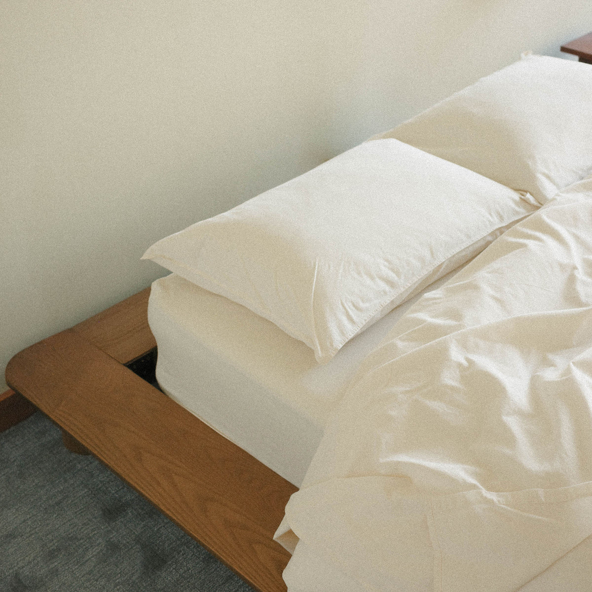 Neatly made bed with cream bedding and pillows on a wooden bed frame.