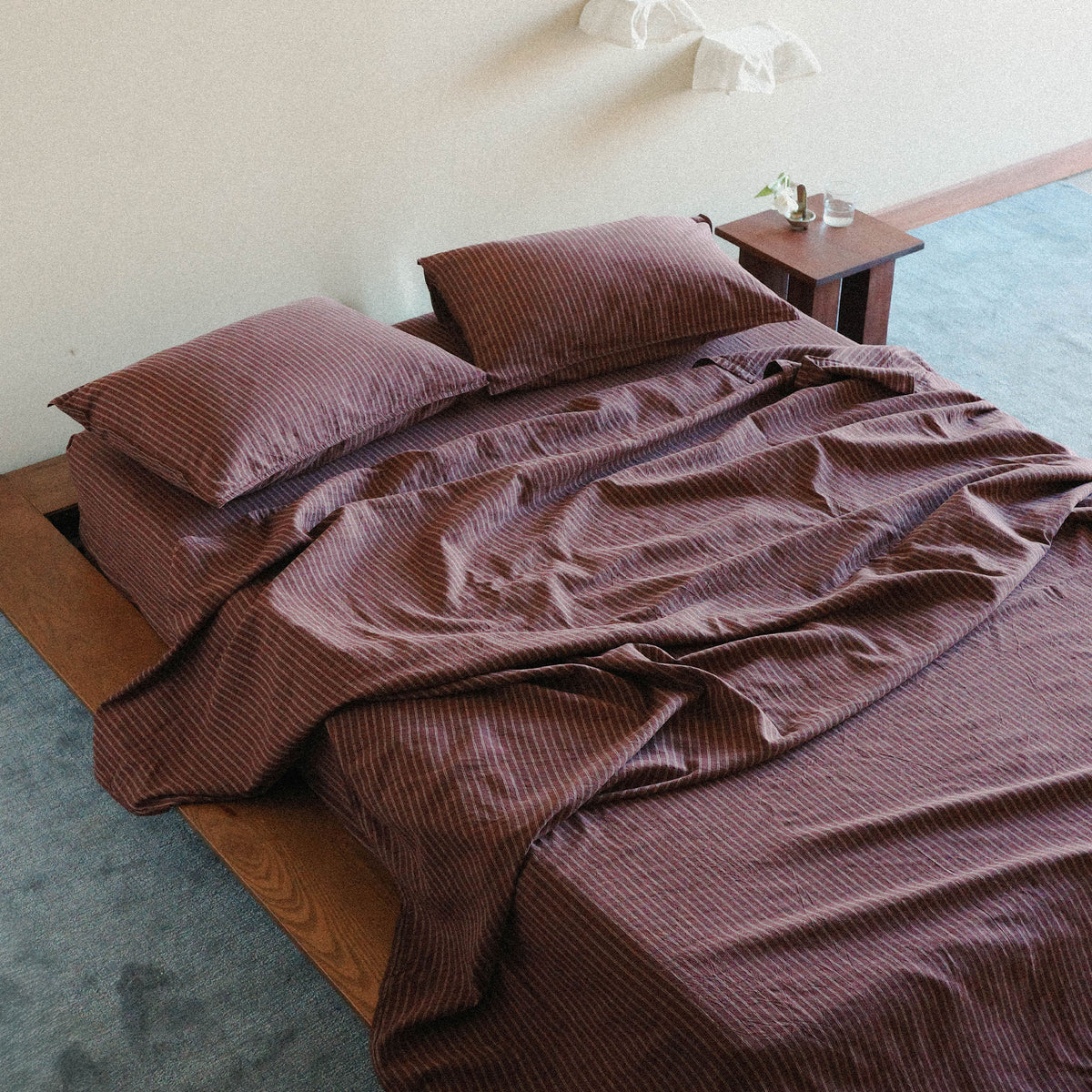 Overhead view of a brown striped bedding set on a bed with a wooden baseboard and a night stand next to the bed with objects on it.