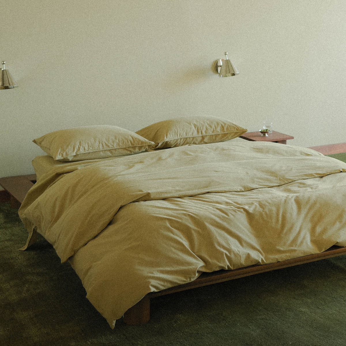 Green duvet cover and pillows on a bed in a room with wall silver sconces.