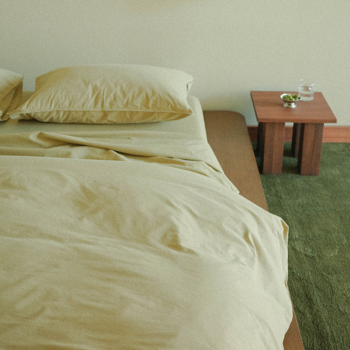 Green duvet cover on a bed with a wooden side table and green carpet.